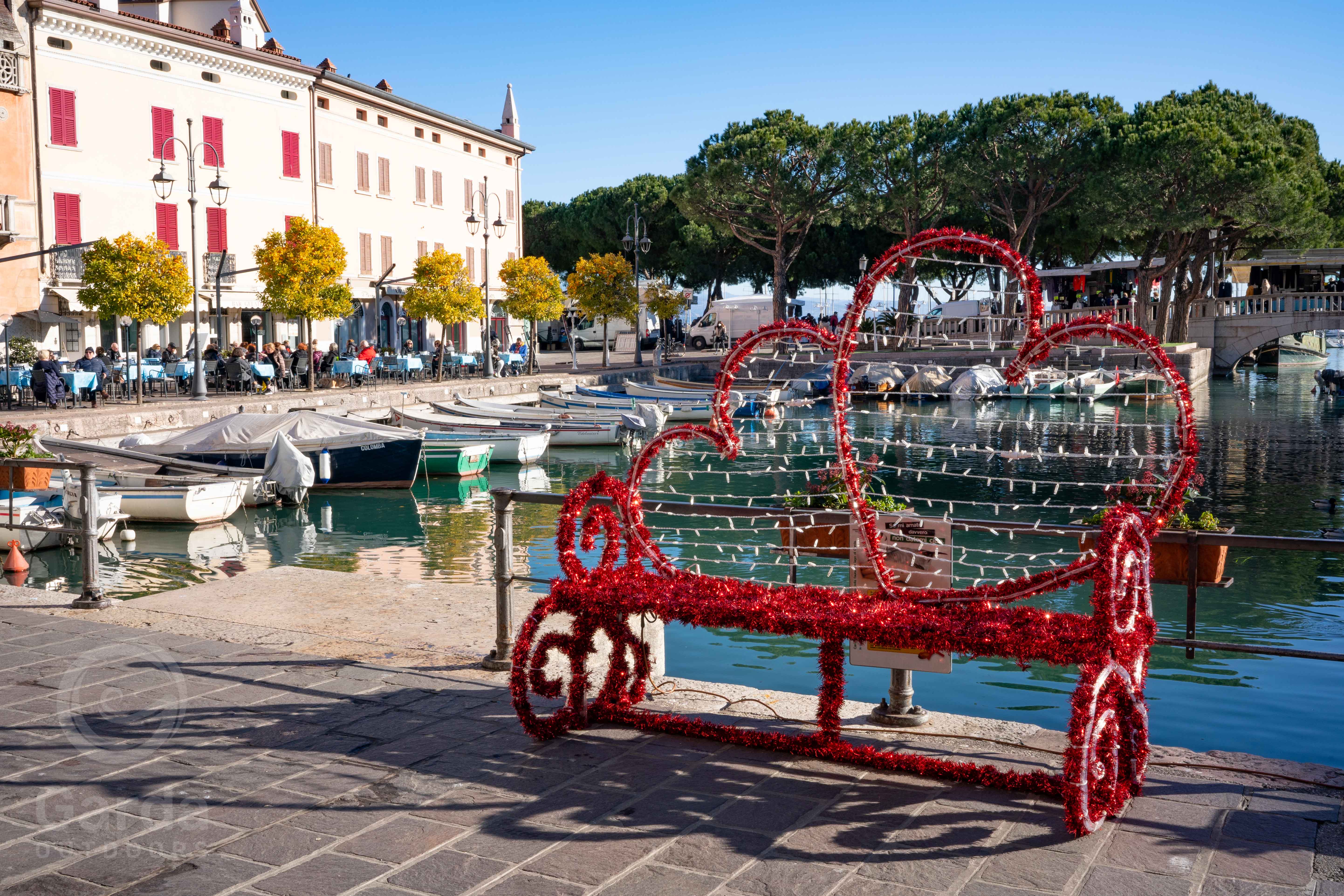 A heart-shaped bench decorated with Christmas lights along the harbor of Lazise on Lake Garda.