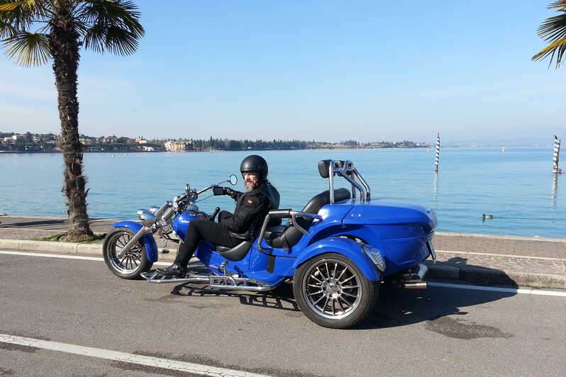 A man riding a blue trike along the promenade with a scenic view of Lake Garda.