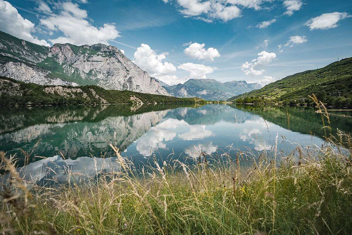 Panoramica del Lago di Cavedine con le montagne circostanti e le nuvole riflesse nelle sue acque tranquille.